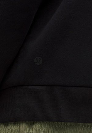 Zwarte stof met een subtiel reliëf Lululemon-logo boven een geribbelde onderrand en groene gestructureerde shorts eronder.