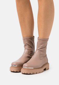 Botines de cuero beige suave con un acabado mate, punta redondeada, suela de plataforma texturizada y un acento metálico en la puntera.