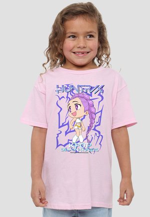 Young girl with curly hair wearing a pink T-shirt featuring a purple-haired chibi character and text "KPOP Demon Hunters."