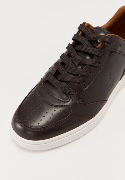 Baskets en cuir marron foncé avec un bout perforé, des coutures contrastantes et des lacets marron. Semelle en caoutchouc blanc avec un branding subtil sur le côté.