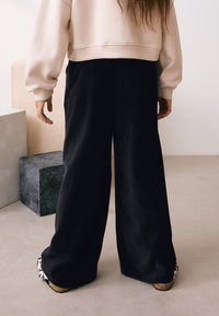 Crne široke hlače s glatkom teksturom, uparene sa svijetloružičastom kratkom majicom. Ističu se masivne cipele s uzorkom.