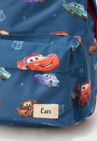 Σακίδιο με μπλε ύφασμα που έχει χρωματιστούς κινουμένους χαρακτήρες αυτοκινήτων, μια ετικέτα με την ένδειξη "Cars" και μια τσέπη με κόκκινες λεπτομέρειες.