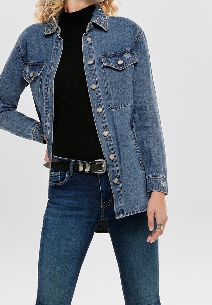 Leren spijkerjack in lichtblauw met zilveren knopen, twee borstzakken, een kraag en lange mouwen, gedragen over een zwarte top en jeans.