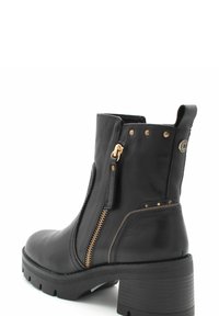 Bota de cuero negro con tacón grueso, cierre lateral, acentos dorados y detalles de remaches cerca de la parte superior, con un diseño de punta redondeada.