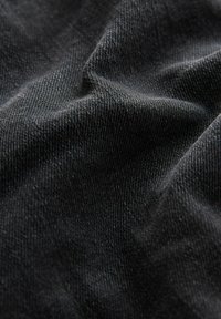 Gros plan sur un tissu en denim noir avec une texture de tissage visible et des plis doux créant des ombres et des reflets.