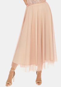 Jasnoróżowa spódnica z tiulu o zwiewnym kroju, z warstwowym efektem i korzystnym fasonem w kształcie litery A, w połączeniu z neutralnymi sandałami na cienkich obcasach.