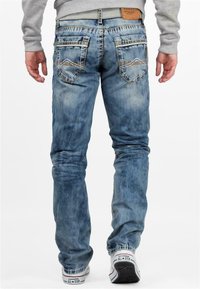 Jeans in denim blu sbiadito con vestibilità slim, caratterizzati da cuciture a contrasto, due tasche posteriori con motivi decorativi e una patch in pelle sulla vita.