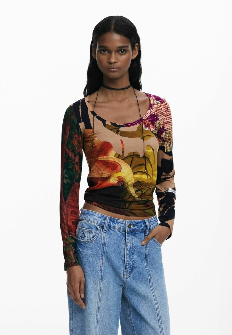 Langærmet top med et flerfarvet blomstermotiv og abstrakt mønster i et blødt stof, kombineret med lyseblå højtaljede jeans.