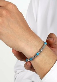 Silverfärgad armband med turkosa och silvriga kulor, med en texturerad design och en låsning på handleden.