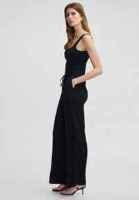 Zwarte mouwloze top met een aangesloten ontwerp, gecombineerd met zwarte wijde broek met een textuurstof en een trekkoord in de taille.