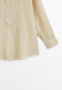Chemise en lin beige à manches longues avec boutons sur le devant et manches à revers, présentée sur fond blanc.