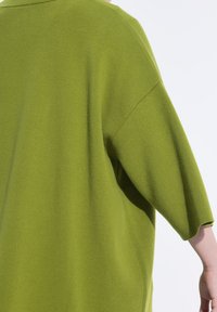 Zelený oversized pletený svetr s uvolněným střihem, širokými rukávy a měkkou texturou. Látka vypadá hladce a má jednotnou barvu.