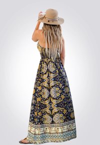 Vestido maxi en azul marino con patrones de paisley florales en dorado y amarillo. Presenta un corpiño fruncido y un dobladillo estampado. Combinado con un sombrero de paja color beige.