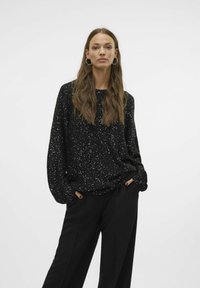 Haut noir à manches longues avec un motif specklé, encolure ronde et coupe décontractée. Associé à un pantalon noir taille haute.