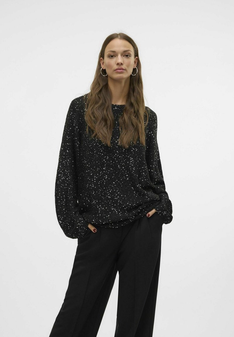 Haut noir à manches longues avec un motif specklé, encolure ronde et coupe décontractée. Associé à un pantalon noir taille haute.