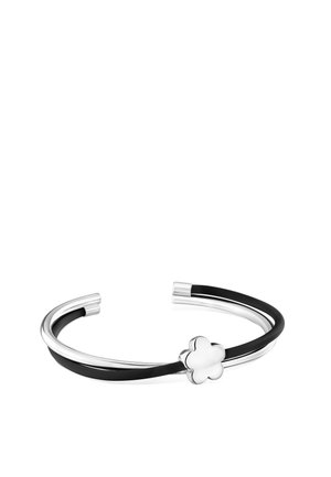 Brazalete abierto de plata con una banda negra y un pequeño charm plateado en forma de flor sobre un fondo blanco.