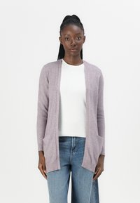 Helllila Cardigan aus weichem Stoff, mit offener Vorderseite, gerippten Bündchen und zwei vorderen Taschen. Über einem weißen Oberteil getragen.