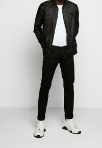 Czarna kurtka bomberka na zamek, biała koszulka, czarne spodnie oraz białe trampki z czarnymi akcentami. Prosty, schludny design i nowoczesny krój.