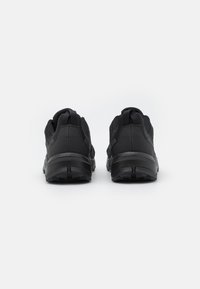Czarne buty sportowe z teksturowanym materiałem górnym, wyściełanym kołnierzem i gumową podeszwą z bieżnikiem zapewniającym przyczepność.