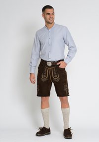 Ruskosuede lederhosen, jossa on koristeellista brodeerausta, paritettu vaaleansinisellä paidalla, vaaleilla polvihousuilla ja tummilla kengillä.
