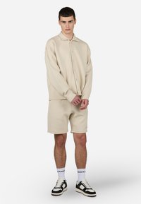 Beige knit button-up shirt with a collar, paired with matching shorts. Features diagonal texture and sporty black and white sneakers.