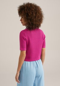 Fuksijas krāsas tamborēta īsām piedurknēm augšdaļa ar noapaļotu dekoltē, kombinēta ar gaiši ziliem plašajiem biksēm. Uz apģērba redzama teksturēta raksts.