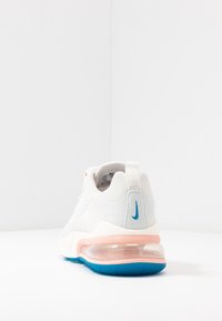 Bílé tenisky Nike viděné ze zadní strany, s viditelnou vzduchovou bublinou a růžovými a modrými akcenty na bílém pozadí.