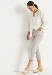 Lätt krämvit blus med broderade ärmar, kombinerad med ljusgrå ankellånga byxor och beige espadrillos med kilklack, med en remdesign.