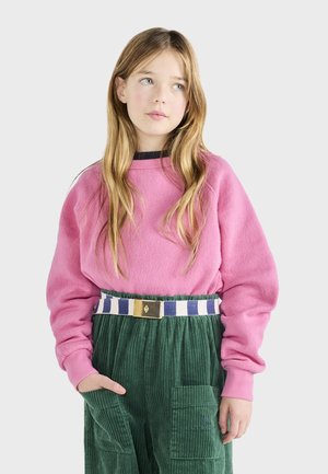 Rosa Fleece-Sweatshirt mit Rundhalsausschnitt und langen Ärmeln, kombiniert mit grünen Cordhosen, die einen gestreiften Gürtel und Taschendetails aufweisen.