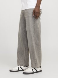 Grå brede jeans lavet af denim med en falmet finish, sidelommer og kontrastsyede detaljer, parret med hvide sneakers med sorte striber.