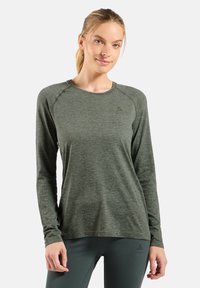 Langärmliges Activewear-Oberteil aus strukturiertem dunkelgrünem Stoff, mit einem runden Halsausschnitt und Raglanärmeln, die ein dezentes Markenlogo auf der Brust aufweisen.