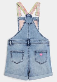 Salopette en denim bleu clair avec des bretelles à logo rose et jaune et un patch logo rose sur la poche arrière droite.