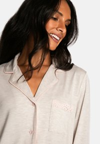 Light gray pajama top with pink piping, featuring a breast pocket adorned with lace trim and a relaxed collar design. Smooth fabric texture.