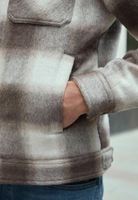 Fleece jacket in shades of brown and beige, featuring a chest pocket, soft texture, side hand pockets, and a relaxed fit.