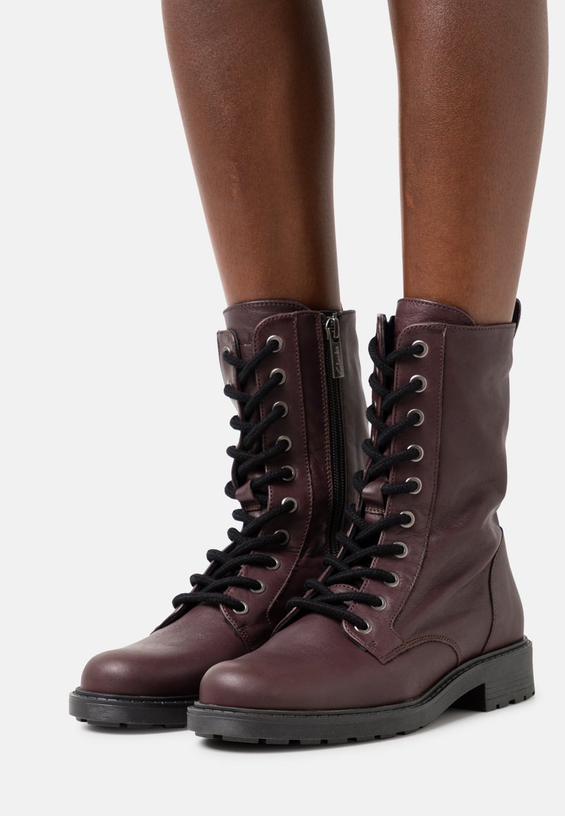 Βουργουνδία δερμάτινες μπότες μέχρι τον αστράγαλο με μαύρα κορδόνια, πλαϊνό φερμουάρ, στρογγυλή μύτη και υφασμάτινη αντιολισθητική σόλα. Διαθέτουν μεταλλικά τρυπήματα και ραφές.