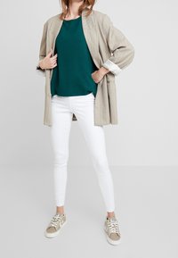 Beige randig kavaj, teal topp, vita skinny jeans och beige sneakers. Kavajen har uppvikta ärmar och en avslappnad passform.