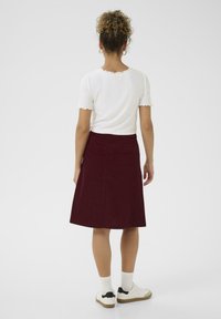 Jupe en velours côtelé bordeaux avec une forme évasée, associée à un haut en maille blanche avec des bords festonnés, et des baskets blanches avec des accents noirs.