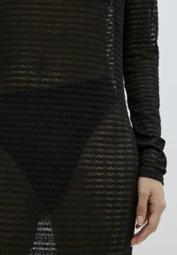 Schwarzes, durchscheinendes Strickkleid mit langen Ärmeln, strukturiertem Muster und hohem Schnitt am Saum. Verfügt über gerippte Manschetten und eine figurbetonte Silhouette.