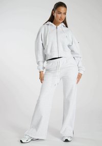Felpa cropped grigia con zip e lacci, abbinata a pantaloni della tuta a gamba larga. Il tessuto sembra morbido e strutturato. Accentuato con scarpe sportive.
