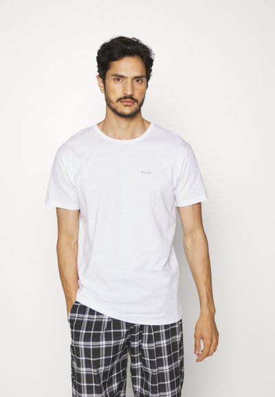 Camiseta de algodón blanca con mangas cortas, escote redondo y un pequeño logo bordado en el pecho; combinada con pantalones de pijama de cuadros en blanco y negro.