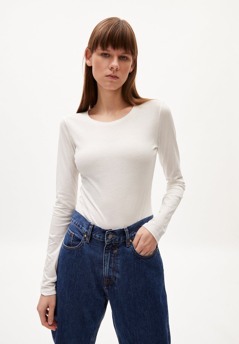 Weißes Langarmhemd aus weichem Material, kombiniert mit hochtaillierten blauen Jeans aus Denim mit Knopfverschluss und Fronttaschen.
