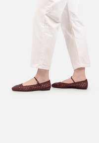 Sandalete croșetate roșii, cu vârful rotund, având o curea subțire la gleznă. Suprafață texturată cu modele decupate și talpă plată neagră.