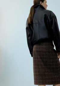 Črna usnjena oversized jakna z visokim ovratnikom, kombinirana z rjavim karo svinčnikom, ki ima strukturiran vzorec in raven kroj.