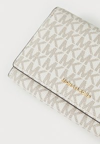Biały portfel z teksturą, z geometrycznym wzorem i złotym logotypem "MICHAEL KORS". Posiada składany design z kontrastującym ciemnym przeszyciem.
