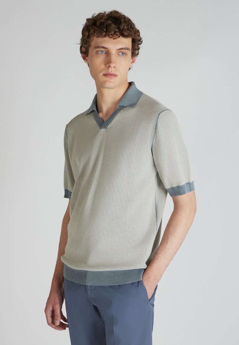 Jasnoszara, dziergana koszulka polo z dekoltem w serek i krótki rękawami. Posiada ciemniejszy szary kołnierz i mankiety oraz fakturowany materiał.