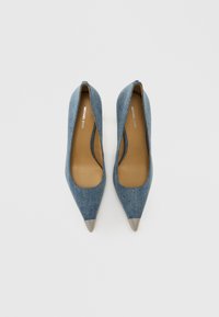 Pantofi cu toc din denim, cu vârfuri ascuțite și părți laterale decupate. Accente metalice argintii pe vârfuri. Căptușeală interioară maro. Design și textură clasică.