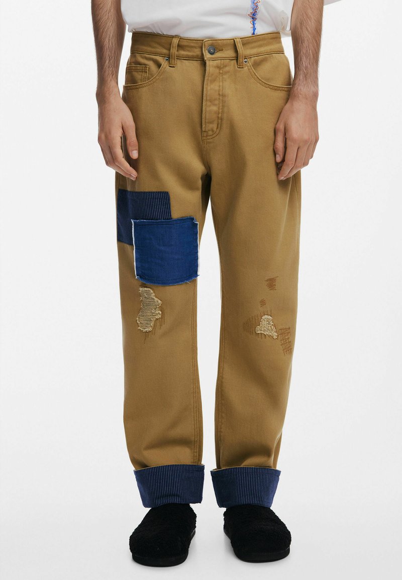 Beiga denimbyxor med blå och manchesterlapp, slitna detaljer och uppvikt nederkant. Har en metallknappstängning och fem fickor.