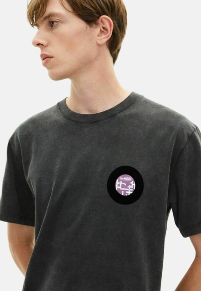 Črno bombažno majico s krožno vijolično grafiko na levem prsnem delu, ki prikazuje pikselizirano zasnovo in besedilo "The Kooples."