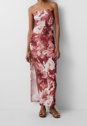 Robe maxi bustier à imprimé floral dans des tons rouges et roses, avec une fente haute jusqu'à la cuisse. Tissu doux et lisse avec une silhouette près du corps.