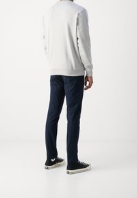 Szary sweter z ściągaczami przy mankietach i u dołu, w zestawieniu z granatowymi spodniami i czarnymi sneakersami z białymi podeszwami i akcentami. Prosty, casualowy design.